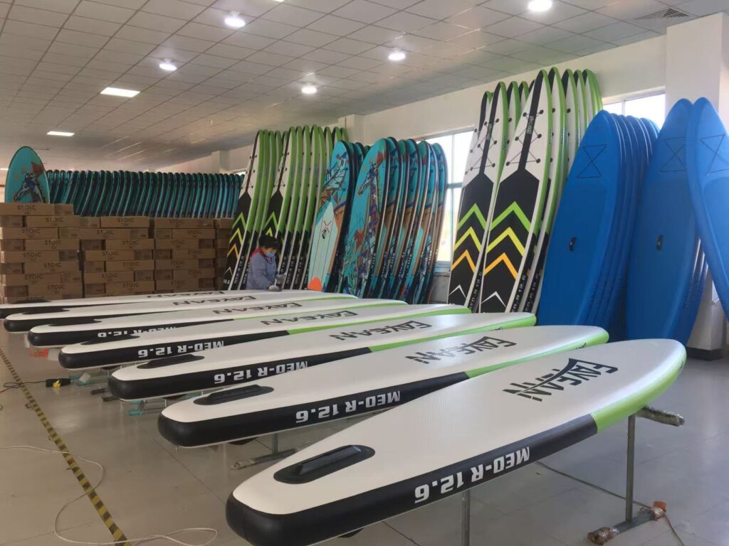 Assorted multi-color inflatable SUP paddleboards stored in a factory warehouse, ready for shipping and distribution